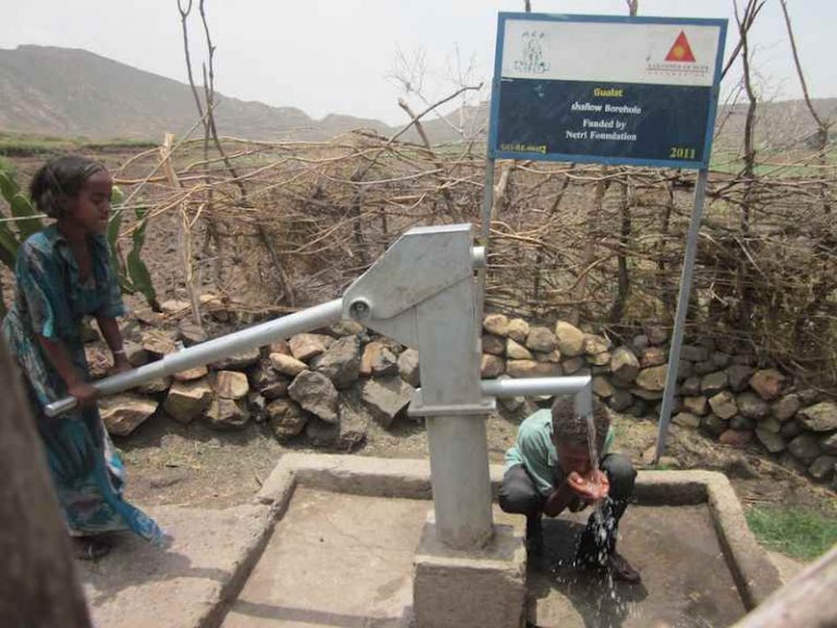 Two young men drink from one of the wells at Robit. Source: A Glimmer of Hope